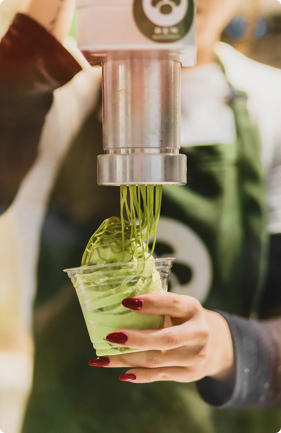 Matcha sauce flows down from a special extruder into a transparent cup. The cup is held in the hand and receives the matcha topping in the form of sauce on top of the matcha cream. Matcha dessert serving process.